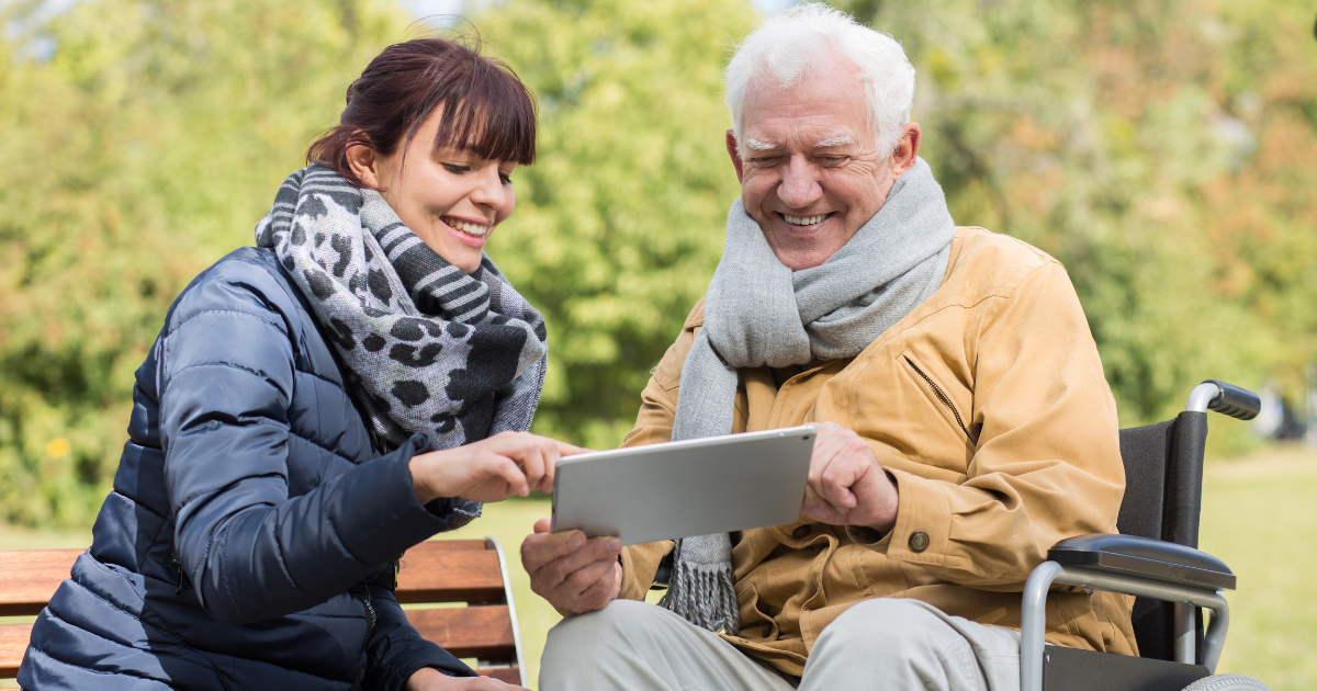Elderly man getting help with his tablet from caregiver