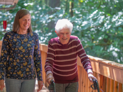 A caregiver walks alongside a smiling senior using a walker outdoors, reflecting supportive live-in care in Albuquerque, NM.